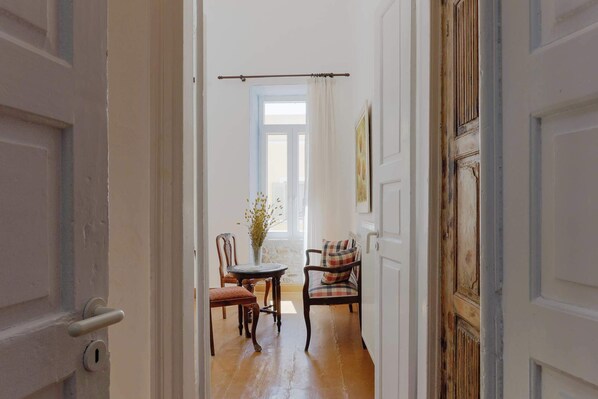 A hallway with a wooden floor, a dining table with chairs, and a window with curtains.