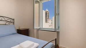 Une chambre à coucher avec un lit, une table de chevet, une fenêtre donnant sur un immeuble et une tour.