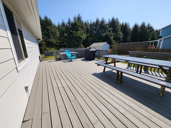 A wooden deck with a picnic table and a blue chair, surrounded by a wooden fence and trees.