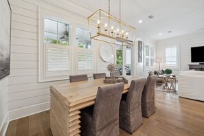 Un comedor amplio con una mesa y sillas de madera, una lámpara moderna y ventanas grandes con persianas.