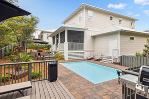 Un patio trasero residencial con piscina, una terraza amueblada y una parrilla para barbacoa.