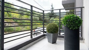 Ein Balkon mit Metallgeländer, einem Blumentopf und Blick auf eine Straße sowie Grünflächen.