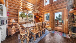A log cabin interior with a dining area, wooden chairs, a chandelier, and a stone wall. - The Broadmeadow Cabin - Vr-25-0005 3 Bedroom Cabin (Lyons)