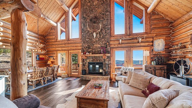A log cabin interior with a stone fireplace, wooden furniture, and large windows. - The Broadmeadow Cabin - Vr-25-0005 3 Bedroom Cabin (Lyons)