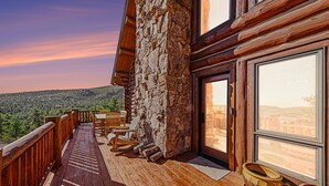 A wooden deck with a stone wall, wooden chairs, and a large window offering a view of a mountainous landscape. - The Broadmeadow Cabin - Vr-25-0005 3 Bedroom Cabin (Lyons)
