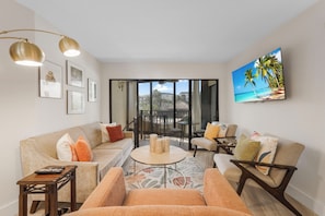 A living room with a sofa, armchairs, a coffee table, and a TV mounted on the wall.