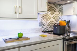 Una cocina con armarios blancos, una tabla de cortar con una manzana, una olla y un cuchillo.