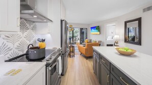 Una cocina moderna con una isla central, un comedor con sofá y un televisor montado en la pared.