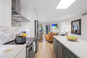 Uma cozinha moderna com uma ilha central, uma sala de jantar com um sofá e uma TV fixada na parede.