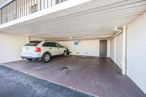 A white car parked in a covered parking garage with a concrete floor and a white wall.