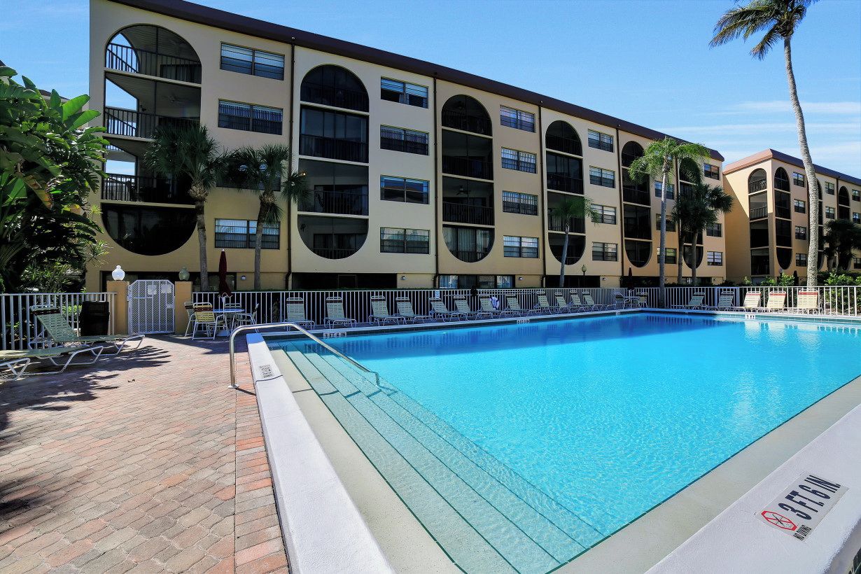 Un hôtel doté d’un espace piscine comprenant une grande piscine rectangulaire, des chaises longues et des palmiers.