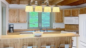 A kitchen with wooden cabinets, a large island with stools, a microwave, and a sink. - Mountainside Getaway (Burke)
