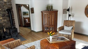 A cozy living room with wicker furniture, a leather ottoman, a bookshelf, and a stone wall with a chimney. - Mountainside Getaway (Burke)