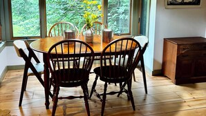 A dining area with a wooden table, four chairs, a hanging light fixture, and a window with a view of greenery. - Mountainside Getaway (Burke)