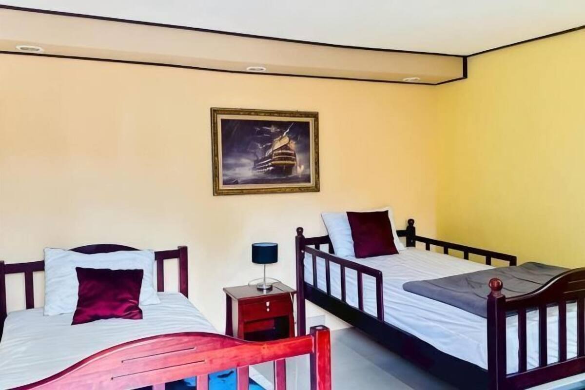 A room with two beds, a nightstand, a framed picture on the wall, and a window.