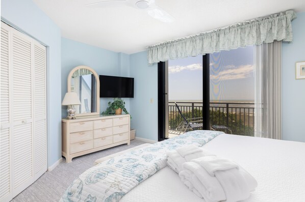 Un dormitorio con cama, cómoda, espejo, televisor y balcón con vistas.