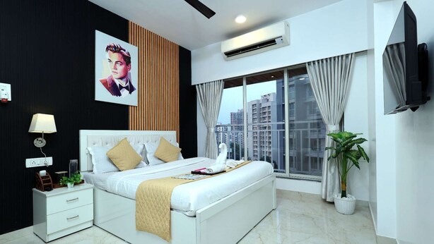 A modern hotel room with a large bed, a TV, a window with curtains, and a potted plant. - 2BHK Master Suite (Gagal Home) (Mumbai)