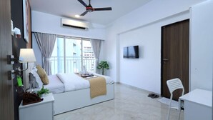 A hotel room with a bed, a desk, a chair, an air conditioning unit, a ceiling fan, a TV, and a window with curtains. - 2BHK Master Suite (Gagal Home) (Mumbai)