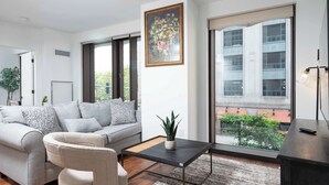 A modern living room with a sofa, a coffee table, and a large window offering a view of buildings and greenery.