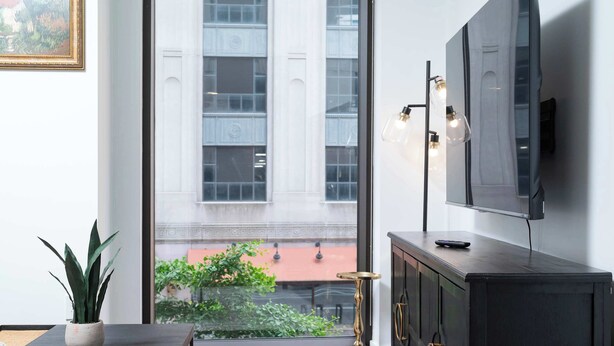 A modern living room with a large window, a dark wooden cabinet, a small round table, and a potted plant.