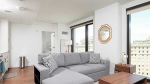 Una sala de estar moderna con un sofá seccional gris, una mesa de centro de madera y un ventanal con vistas a la ciudad.