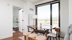 Un comedor moderno con una mesa y sillas de madera, un ventanal con vista a la ciudad y una puerta blanca que da a otra habitación.