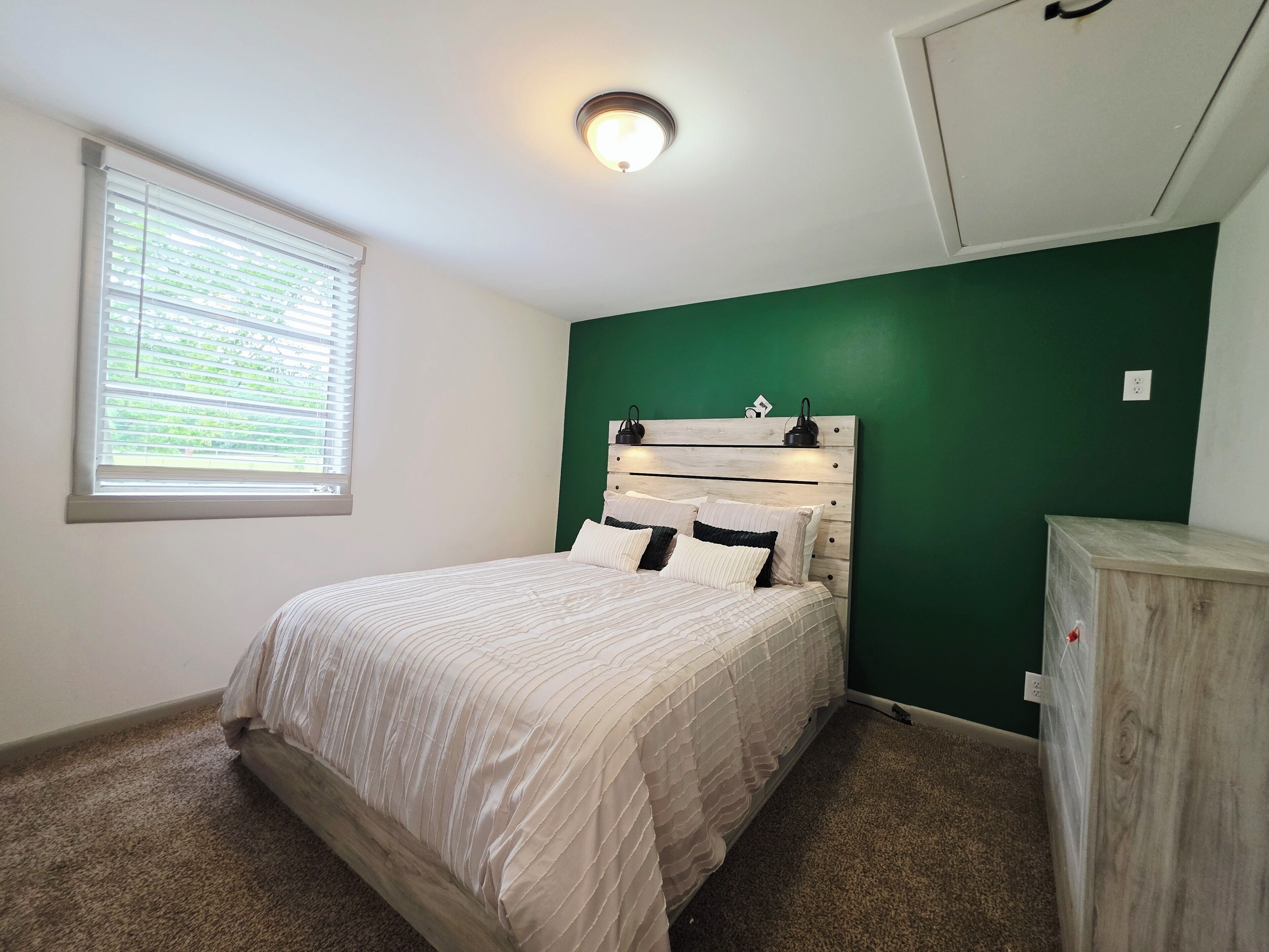 Une chambre à coucher avec un lit, une fenêtre avec des stores, un mur vert et une armoire en bois.