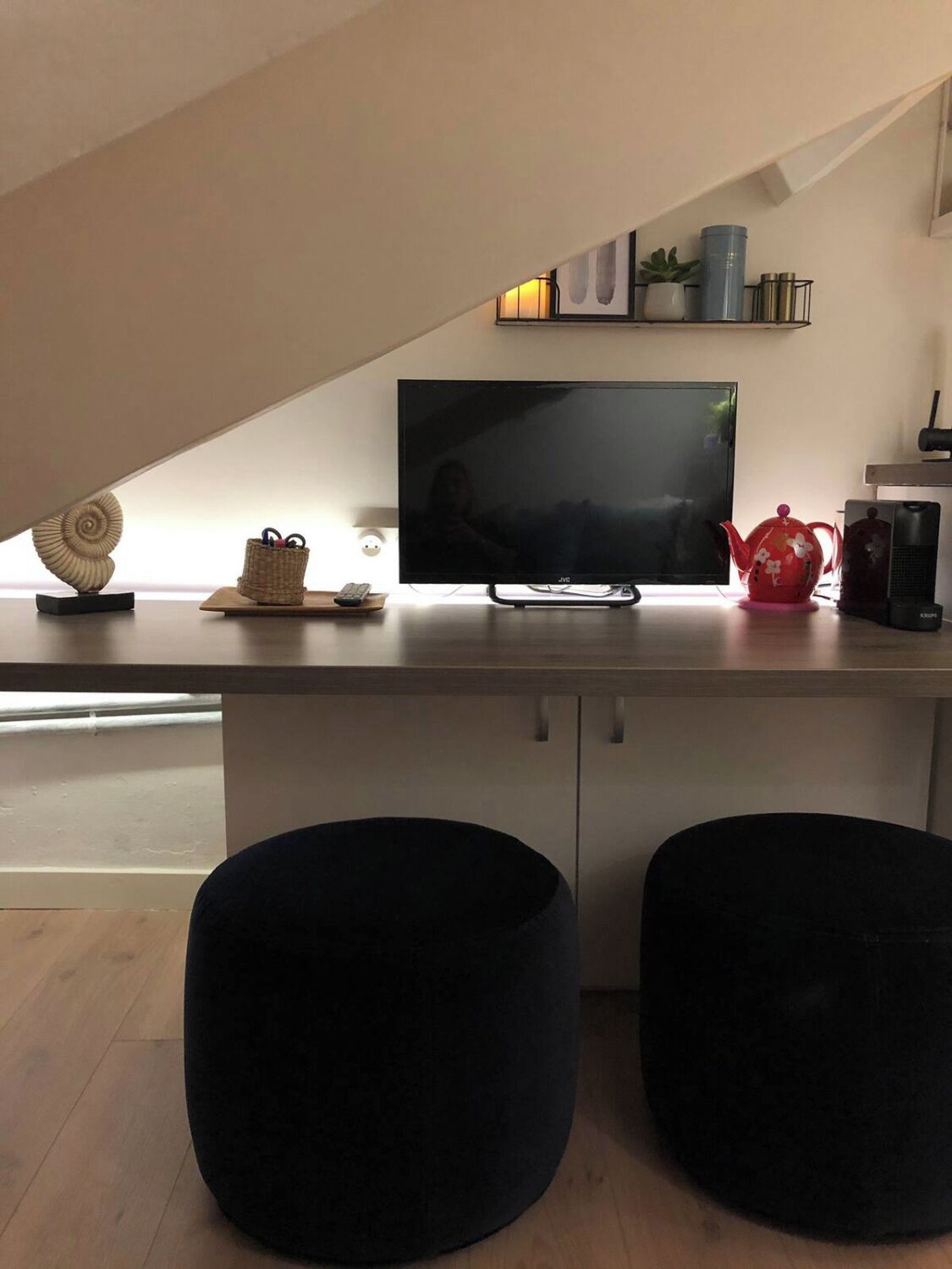 A modern living space with a flat-screen TV on a white cabinet, a red teapot, and two black ottomans.
