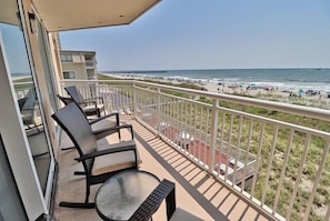 A balcony with a view of the beach, equipped with chairs and a table.