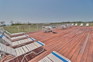 A wooden deck with lounge chairs and tables, overlooking a grassy area. - Oceanfront 3BR Family Condo with Pool and Views (North Myrtle Beach)