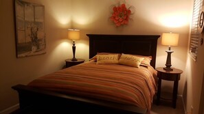 A bedroom with a bed, two bedside tables with lamps, a wall clock, and a floral decoration.