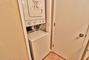 A compact laundry room with a washing machine and dryer, a door, and a carpeted floor.