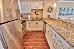 A kitchen with white cabinets, a stainless steel refrigerator, granite countertops, and a wooden floor. - Oceanfront 3BR Family Condo with Pool and Views (North Myrtle Beach)