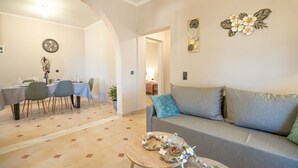 Ein Wohnzimmer mit grauem Sofa, einem Esstisch mit Stühlen und einem kleinen runden Tisch mit einem dekorativen Kranz.