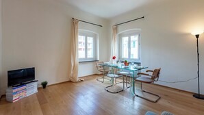 A modern living room with a glass dining table, metal chairs, a flat-screen TV, and a floor lamp. - Lovely House in Boccadasse (Genoa)