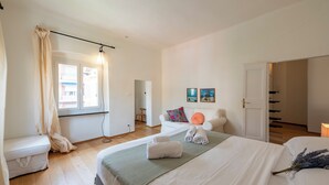 A modern bedroom with a large bed, a bedside table, a window with curtains, a chair, and a door leading to another room. - Lovely House in Boccadasse (Genoa)