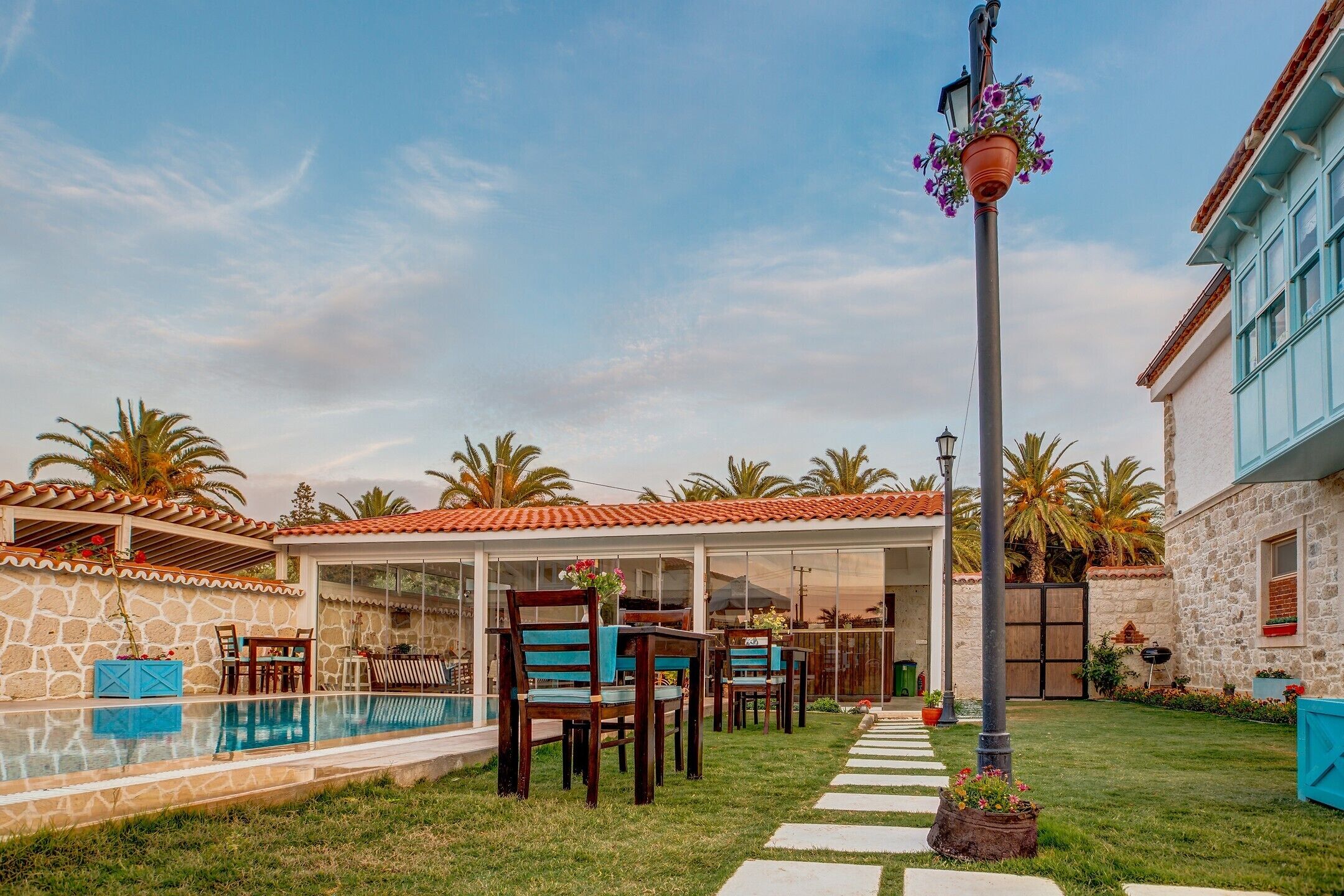 Un espace aménagé au bord de la piscine, avec un coin salon abrité, un mur en pierre et un ciel dégagé.