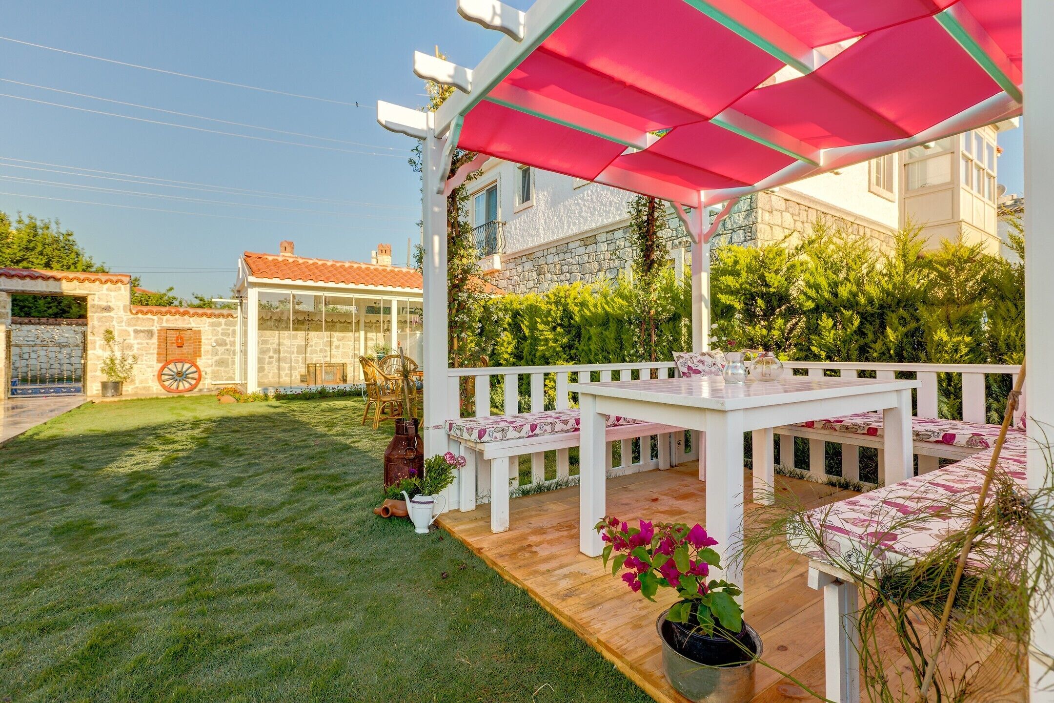 Une terrasse avec une table et des bancs blancs, entourée d’une clôture blanche et d’un auvent rose.