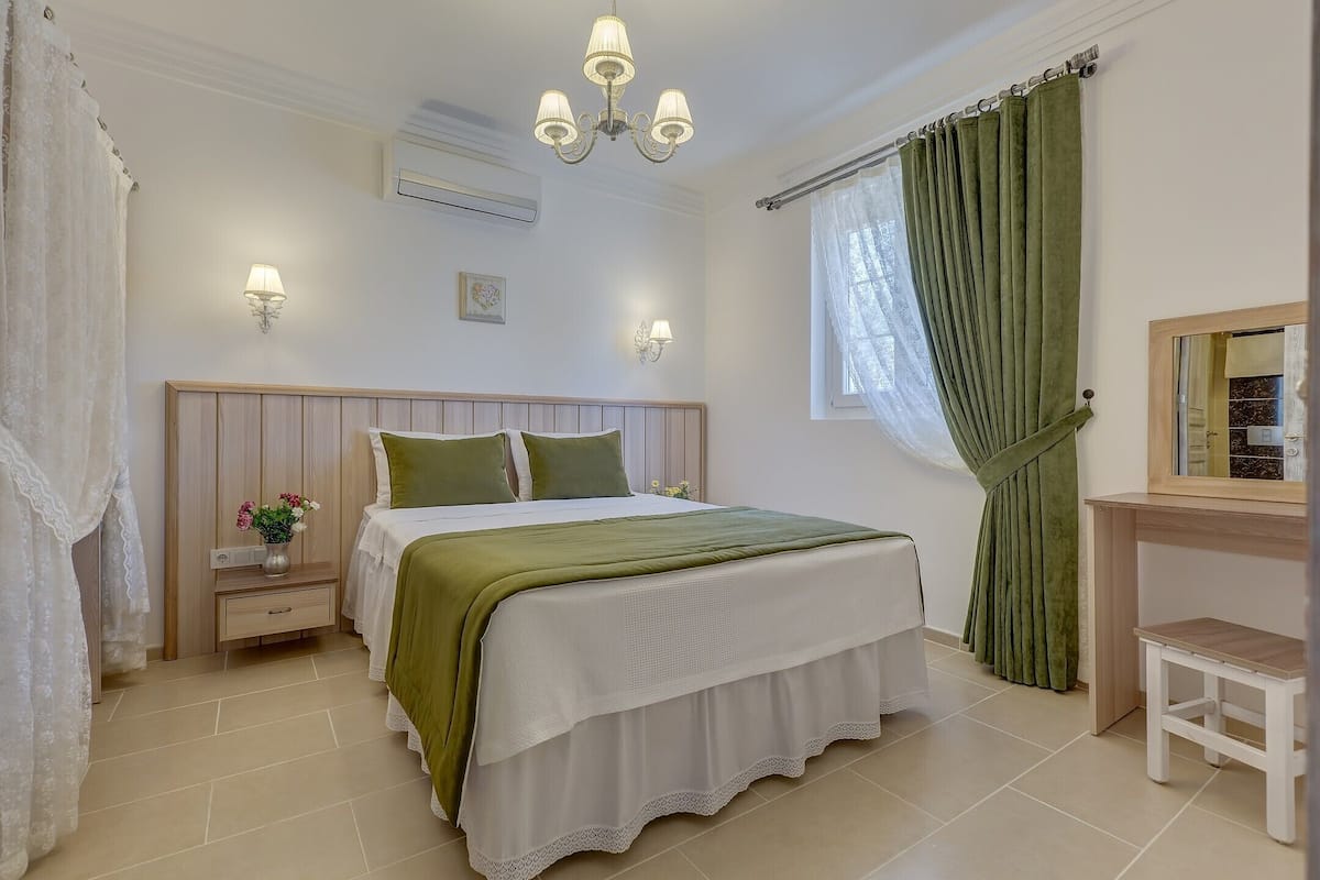 A bedroom with a bed, bedside tables, a nightstand, a mirror, and a window with curtains.