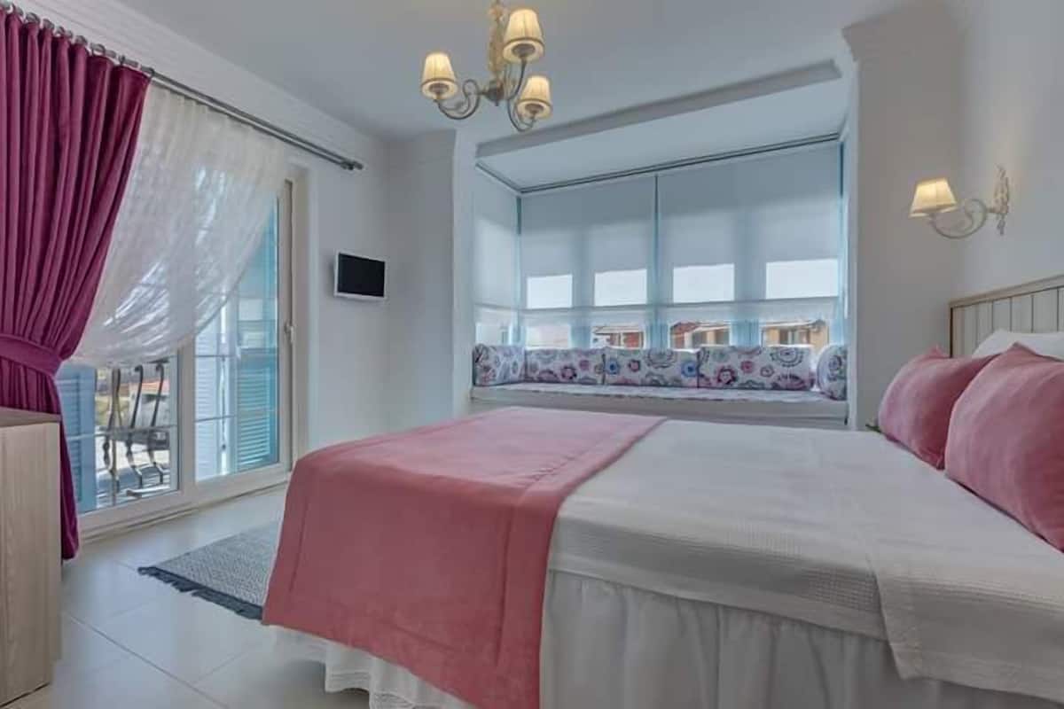 A bedroom with a large bed, a window with a view, and a chandelier.