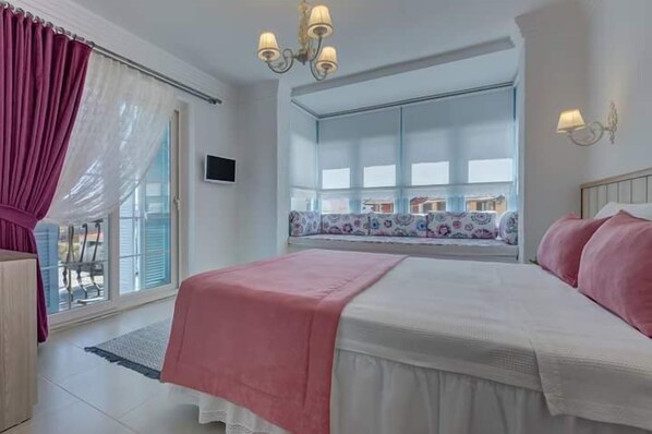 A bedroom with a large bed, a window with a view, and a chandelier. - Bella pietra otel (Cesme)