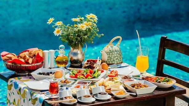 Ein Tisch mit verschiedenen Frühstücksangeboten, einer Blumenvase und einem Glas Orangensaft an einem Pool.