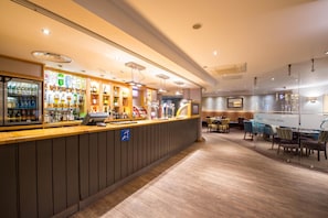 A bar area with a counter, shelves of bottles, and a seating area with tables and chairs. - Premier Inn Liverpool City Centre - Moorfields (Liverpool)