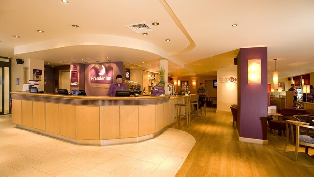 Un espace d’accueil d’hôtel avec un comptoir incurvé, une horloge et un panneau indiquant « Premier Inn ».