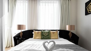 Habitación de hotel con una cama bien hecha, dos lámparas de noche y una disposición de toallas en forma de corazón sobre la cama.
