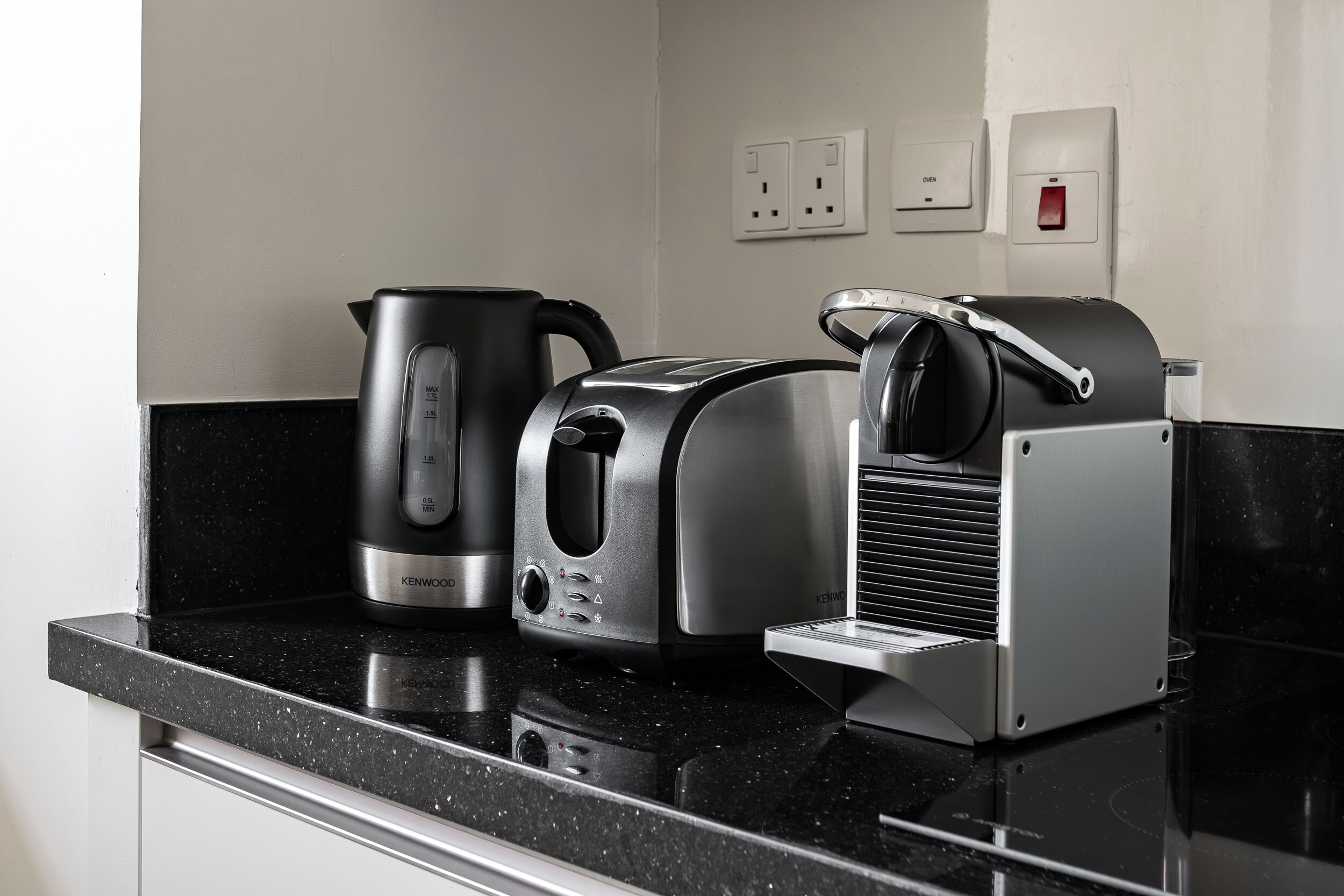 A kitchen with a black countertop, a coffee maker, a toaster, and a bread maker.