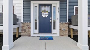 Una puerta principal con un letrero que dice 'Serenity Starfish House' y un felpudo que dice 'VAY YOU'RE HERE!'.