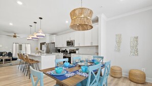 Una cocina moderna con armarios blancos, una isla central y un comedor con sillas azules y una mesa de madera.