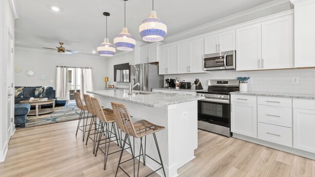 Una cocina moderna con armarios blancos, electrodomésticos de acero inoxidable y una isla central con taburetes de bar.