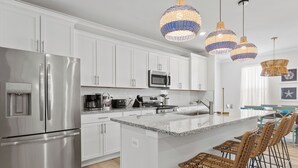 Una cocina moderna con armarios blancos, electrodomésticos de acero inoxidable, encimera de granito y taburetes de mimbre.